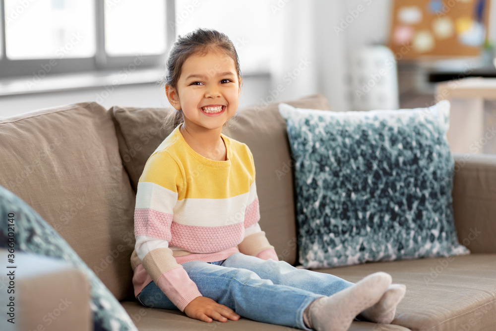 people and childhood concept - happy smiling little girl sitting on sofa at home people and childhood concept - happy smiling little girl sitting on sofa at home