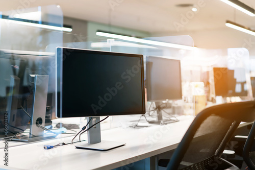Acrylic plexiglass separator setting on the desk with monitor in the office. New normal Concept for social distancing in offices during the Covid-19 pandemic. Precaution and safe.