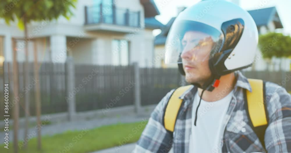 Close up of Caucasian delivery man wearing a safety helmet riding on the scooter. Attractive young male courier elivering the online order to the customer house. E-commerce, Internet shopping. Close up of Caucasian delivery man wearing a safety helmet riding on the scooter. Attractive young male courier elivering the online order to the customer house. E-commerce, Internet shopping.