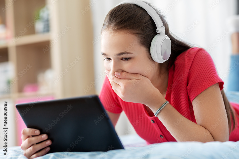 children, technology and communication concept - embarrassed teenage girl in headphones listening to music on tablet computer at home children, technology and communication concept - embarrassed teenage girl in headphones listening to music on tablet computer at home