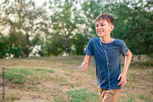 A teenage boy runs in nature with headphones listening to music. Active lifestyle of children and sports.