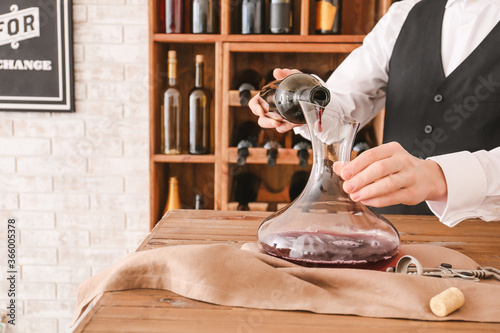 Fotografie Sommelier pouring wine from bottle into decanter in cellar