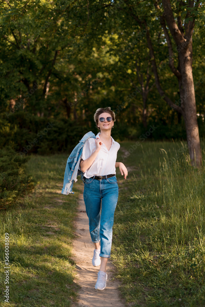 Joyful young woman in fashionable sunglasses walking in nature on a beautiful day Joyful young woman in fashionable sunglasses walking in nature on a beautiful day