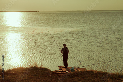 Beautiful sunset over the river with reflection in the water. A fisherman with a fishing rod settled down on the shore.