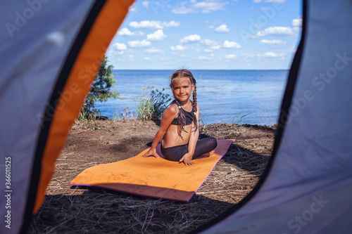 Mental and physical health, safe active lifestyle. Girl doing yoga in campsite on bank of the see © Maria