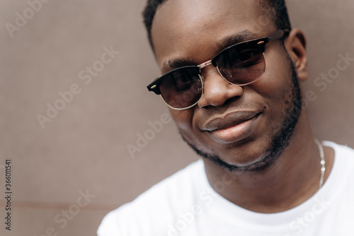 Close up male portrait. Handsome african american guy in a white t-shirt and in sunglasses posing and smiling