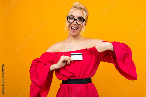 European girl in a red elegant dress with a credit card for shopping in hands with a mockup on a yellow studio background © Ivan Traimak