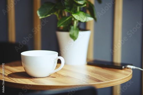 Empty white cup and smart phone on table in cafe. Morning light falls from the window.Coffee break.Blurred image selective focus