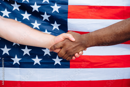 Equality of Nations. Handshake of male hands. Handshake of a Caucasian man and an African on the background of the USA flag