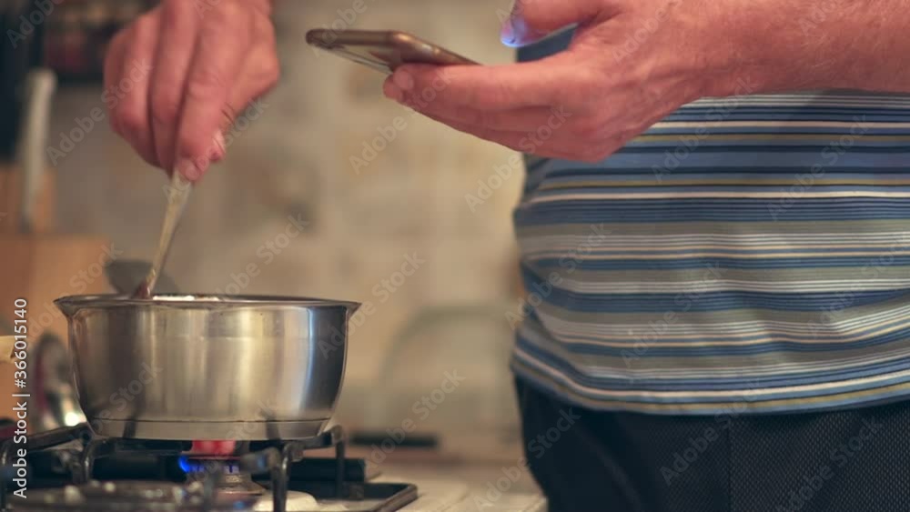 Man mixing chocolate cream on a metallic pan, looking in mobile phone for recipe Man mixing chocolate cream on a metallic pan, looking in mobile phone for recipe