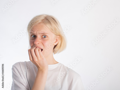 a young blonde girl in a white t-shirt bites her fingernails due to stress/excitement. isolate on white. space for text