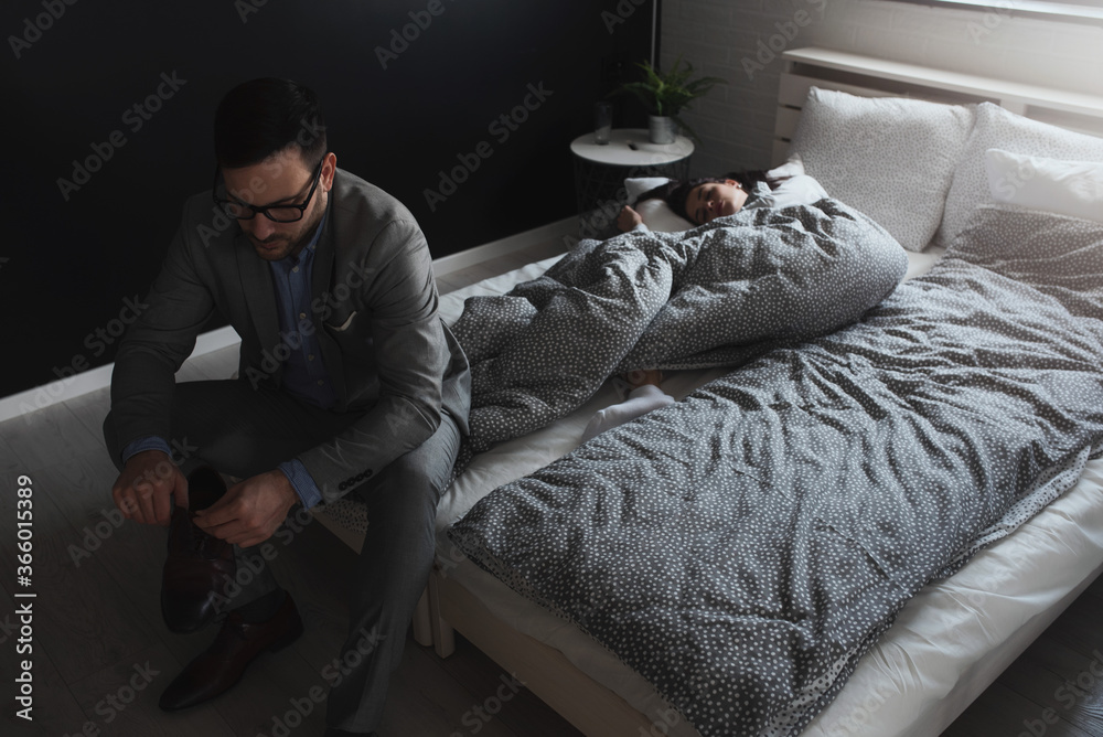 Young couple in bedroom in the morning. Woman is in the bed, and man is going to work. When Work Interferes with Love.