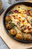 Mouthwatering pub dish, cast iron: baked baby potato with chicken and cheese crust, very close up