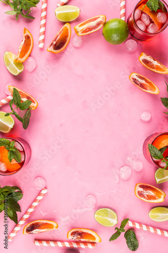 Pink background with ingredients for summer iced red cocktail with blood orange and lime. Vertical