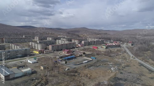 Aerial view of Karabash city with three-story and five-story houses. Cars drive along the road. Spring, trees without leaves. At the background the Ural mountains. Russia, Chelyabinsk region
