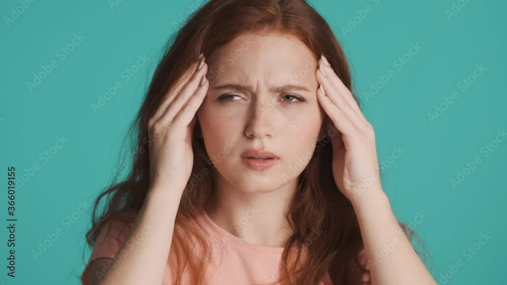 Close up sick redhead girl sadly showing headache on camera over colorful background