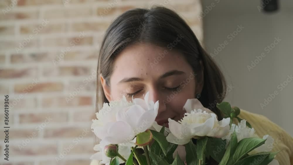 Young pretty cute woman indoors at home with beautiful flowers while smelling them