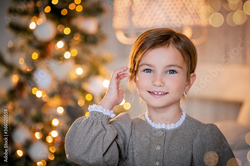 portrait of a child girl smiling. in the background in blurred focus christmas tree glows with garlands, bokeh