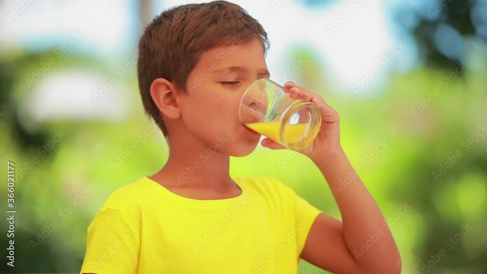 Happy boy in a yellow t-shirt is drinking fresh orange juice outdoors Happy boy in a yellow t-shirt is drinking fresh orange juice outdoors