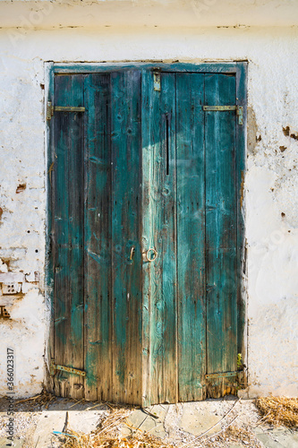 An old turquoise wooden door from a white shed with vintage charm. © Anna