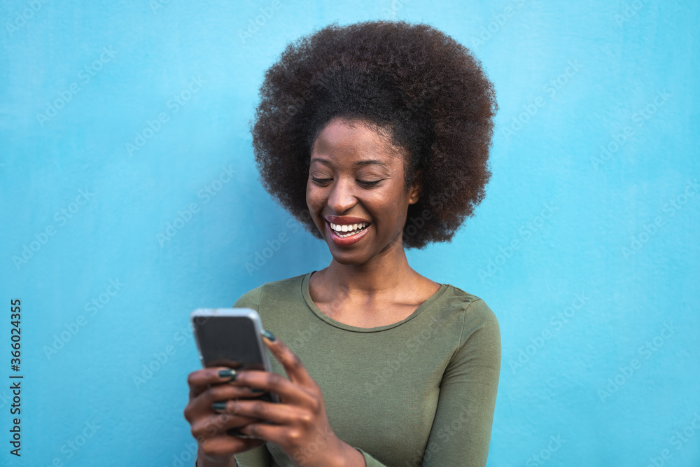 Young Afro woman using mobile smartphone - Happy African girl having fun with new trends technology apps - Youth millennial generation z and social influencer concept - Blue background Young Afro woman using mobile smartphone - Happy African girl having fun with new trends technology apps - Youth millennial generation z and social influencer concept - Blue background