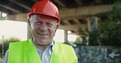 Portrait of handsome senior railroader smiling into camera at railway in summer