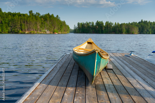 Green canoe rest on a lake wooden pier on a sunny summer day at the cottage. A wood pier is visible across the water.