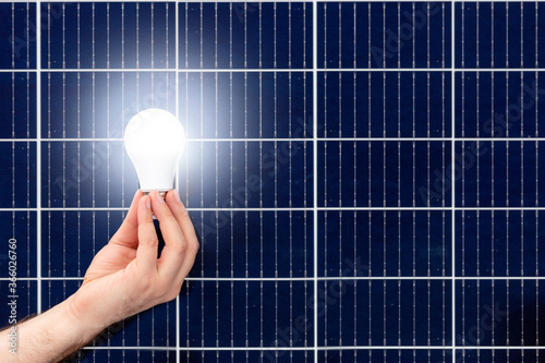 Fototapeta Naklejka Na Ścianę i Meble -  Hand holding white light bulb against solar panel, solar station. Idea concept of alternative energy, technology, environment, ecology. Green power energy. Copy space