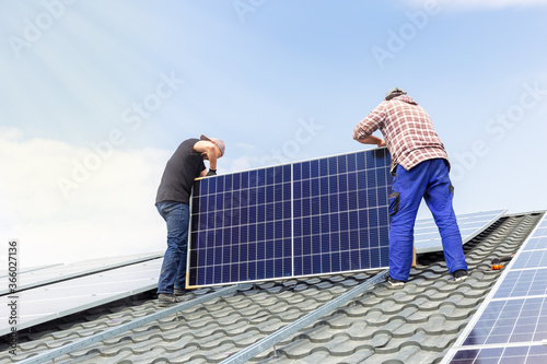 Electrical engineers mans are working installing solar panels on solar station on house roof against blue sky in sunny day. Development sun alternative energy technology. Ecological concept.