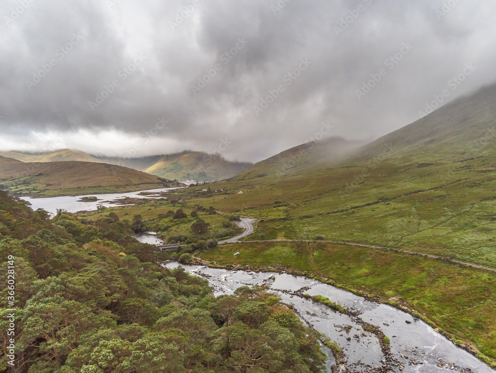 Aerial drone view on a landscape in Connemara region. county Mayo. Ireland, Small river flows from mountain by a forest, Cloudy sky.