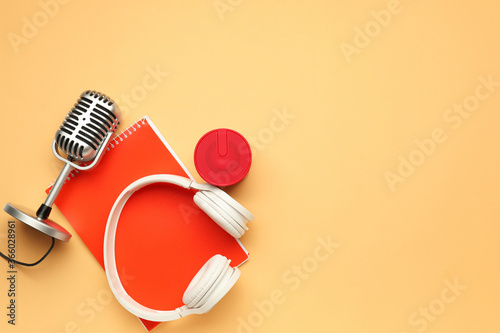 Headphones with microphone, notebook and speaker on color background