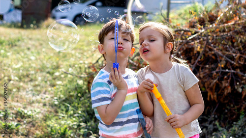 Happy kids blowing bubbles outdoors in the park.Lovely Caucasian children having fun  blowing bubbles. Carefree childhood concept.Portrait of brother and sister standing outdoors and playing together.