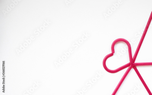 Pink coat hangers are stacked on top of each other in a heart shape in the right corner on a white background 