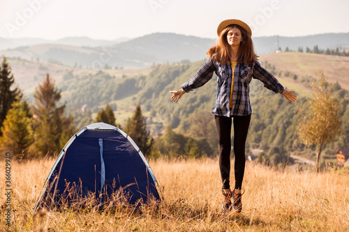 Young beautiful woman in blue shirt and straw hat near tent at autumn landscape background