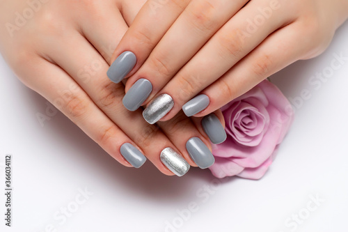 gray manicure with silver sequins on ring fingers on square long nails close-up on a white background with a pink rose in hands