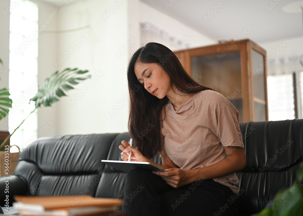 A woman is using a computer tablet and stylus pen while sitting on a black leather sofa. A woman is using a computer tablet and stylus pen while sitting on a black leather sofa.