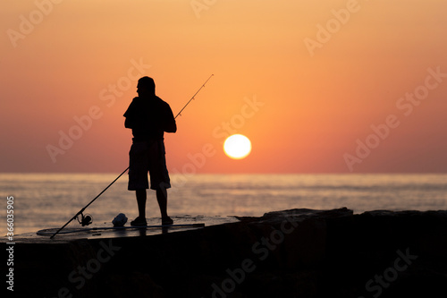 The silhouette of a fisherman standing on the rocks during the sunrise