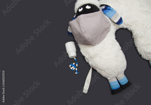 covid 19. travel pillow in the form of a sheep in a protective mask, a thermometer and pills lie on a black background