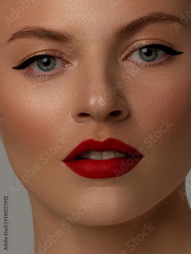 Close-up beauty of a female face with fashion evening make-up. Black liner on the eyes and extremely long eyelashes  on full lips matte scarlet lip color. Well-groomed skin after spa. red lipstick