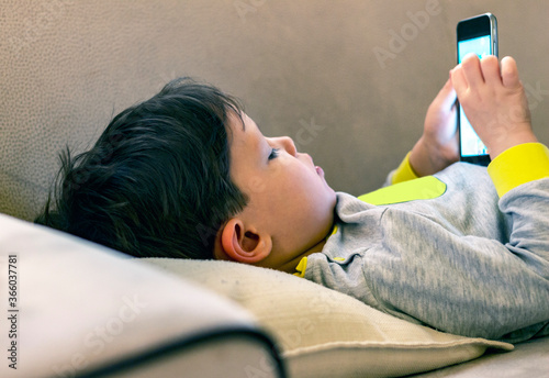 Boy playing smartphone on bed, watching smartphone, young boy use phone and play game, child use mobile, addicted game and cartoon, boy play phone.