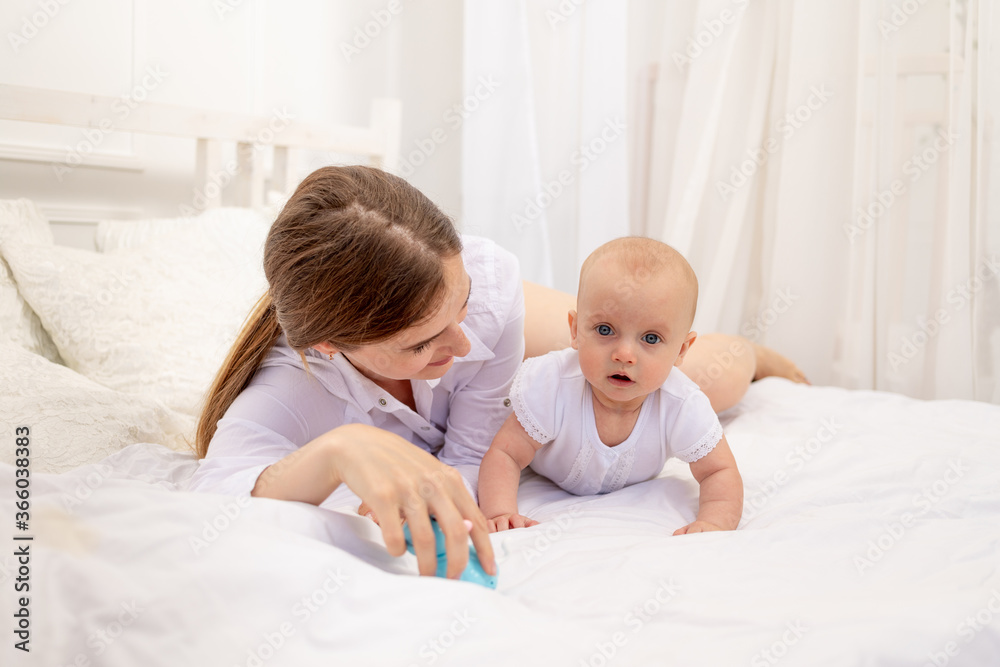 mom playing with baby 6 months lying on a white bed, leisure mom with baby, place for text mom playing with baby 6 months lying on a white bed, leisure mom with baby, place for text