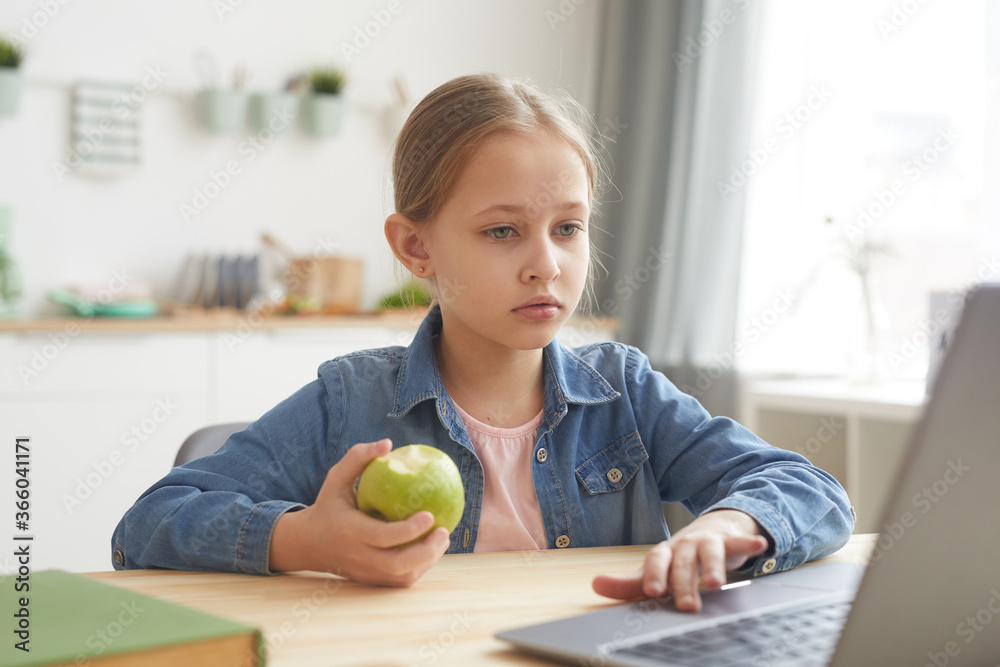 Portrait of cute girl using laptop and eating apple while studying online at home in cozy interior , copy space Portrait of cute girl using laptop and eating apple while studying online at home in cozy interior , copy space