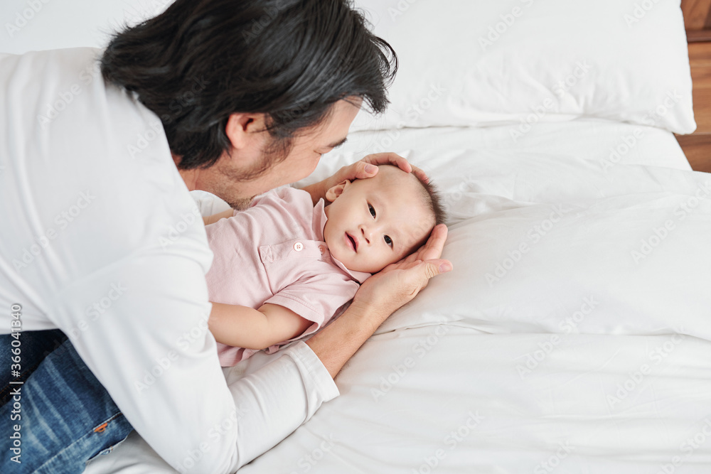 Young father playing with his little son lying on bed and trying to make him sleep Young father playing with his little son lying on bed and trying to make him sleep