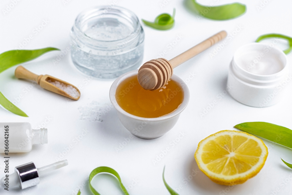 Natural organic ingredients to make home skin care. Cleansing and nourishing cosmetics. Beauty products: cream, honey, sea salt among green leaves on white background. Close up, copy space for text