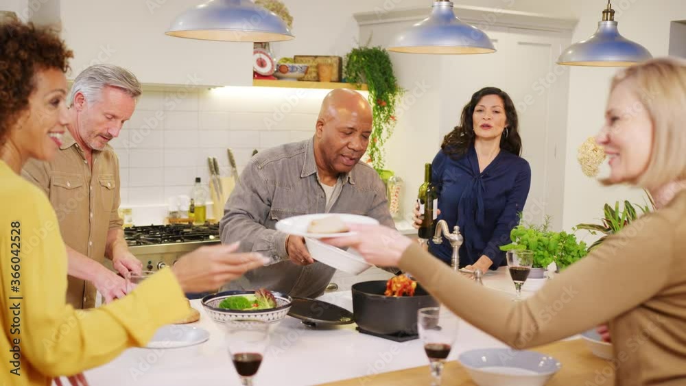 Group of mature friends meeting at home serving food in kitchen together - shot in slow motion Group of mature friends meeting at home serving food in kitchen together - shot in slow motion