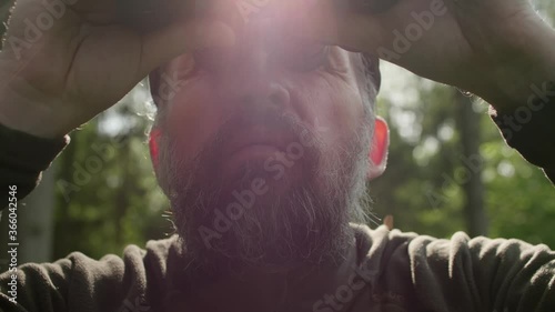 Male hunter in camouflage looks at something attentively and uses binocular. Concentrtion and attention.