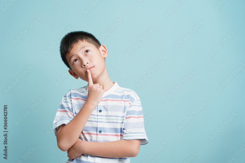 Asian little boy standing thinking on blue background isolated Asian little boy standing thinking on blue background isolated