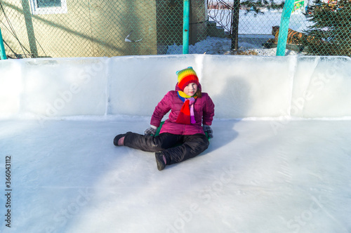 Child rolls down an ice slide. Bright clothes rainbow hat.