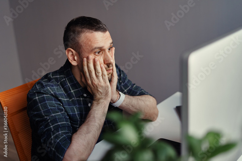 Thoughtful serious young man lost in thoughts in front of laptop, focused entrepreneur or absent-minded student thinking of problem solution