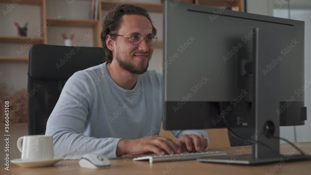A pleased young businessman is typing something on his computer sitting in the office A pleased young businessman is typing something on his computer sitting in the office